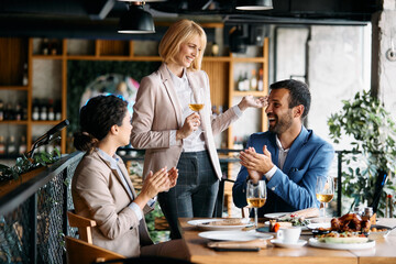 Happy businesswoman holding a toast while colleagues are applauding her during lunch in restaurant.