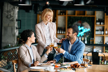 Happy business colleagues toasting with wine while having lunch in restaurant.