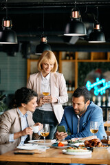 Happy businesswoman and her colleagues using smart phone in restaurant.