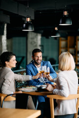 Happy colleagues celebrating success and toasting with wine during business lunch in restaurant.