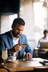 Smiling entrepreneur using credit card and digital tablet while e-banking in cafe.