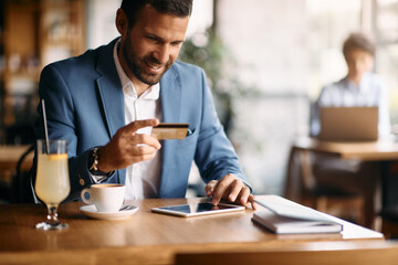 Happy businessman using touchpad while online banking in cafe.
