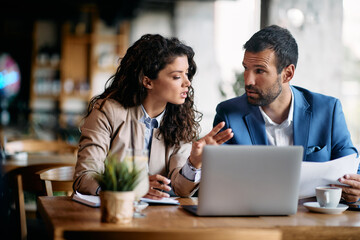 Businesswoman and her colleague talking while going through reports and using laptop in cafe.