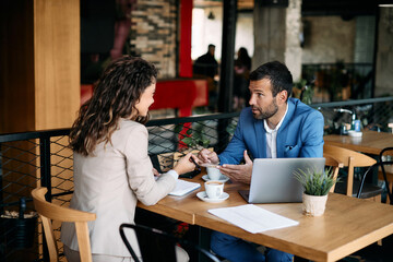 Businessman talking to female colleague and drinking coffee during meeting in cafe.
