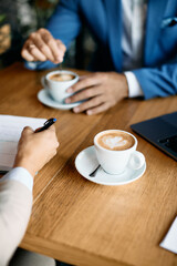 Close up of business colleagues drinking coffee while having meeting in cafe.