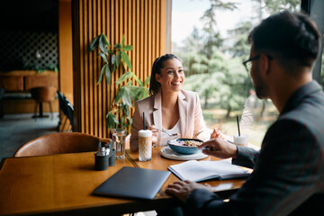 Happy businesswoman talks to colleague while eating breakfast in cafe.