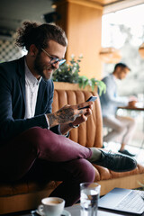 Young happy businessman texting on mobile phone in cafe.