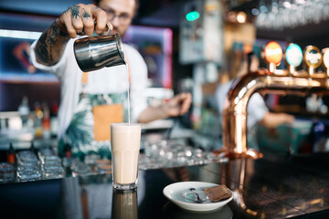 Close up of barista preparing latte coffee in tall drinking glass.