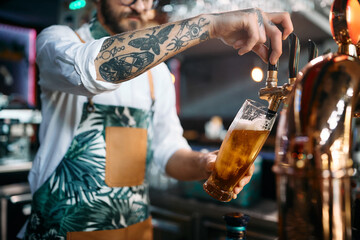 Close up of bartender pouring lager beer from beer tap at bar counter.