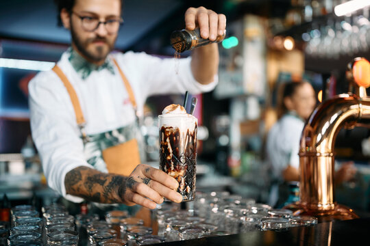 Close up of barista adding cinnamon while making iced coffee at bar counter.