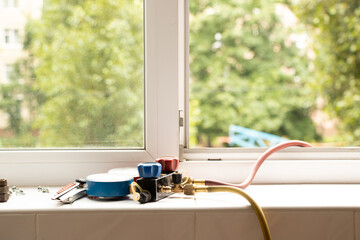 A two-valve manometric manifold lies on the windowsill in the apartment and measures the pressure in the air conditioner at home, repair and diagnostics of the air conditioner - obrazy, fototapety, plakaty