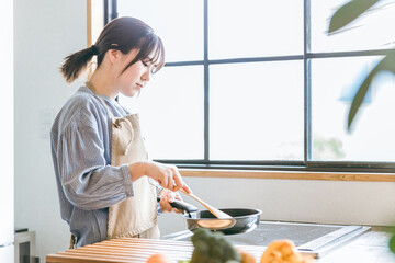 キッチンでフライパンを使う女性（疲れる）  © buritora