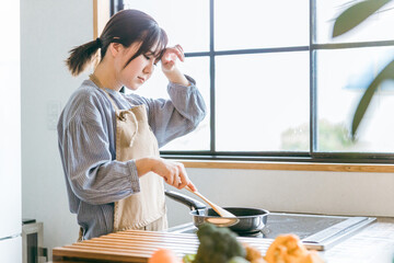 キッチンでフライパンを使う女性（疲れる）
