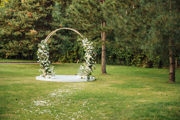 Circle wedding arch decorated with white flowers and greenery outdoors.