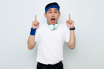 Shocked young Asian sportman in blue headband and sportswear white t-shirt with headphones, pointing fingers up having a good idea isolated on white background. Workout sport concept