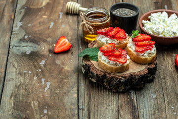 toasts or bruschetta with strawberry and mint on cream cheese ricotta on a wooden background. Delicious breakfast or snack, top view