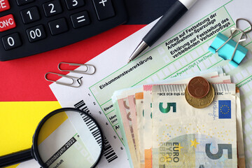 German income tax return form with pen and european euro money bills lies on flag close up....