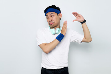 Serious young Asian sportman in blue headband and sportswear white t-shirt with headphones, showing...