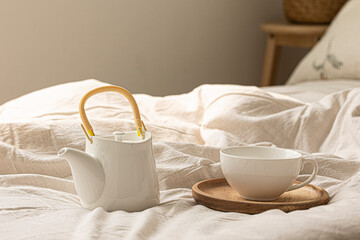 There is a white teapot and a cup on the bed.
