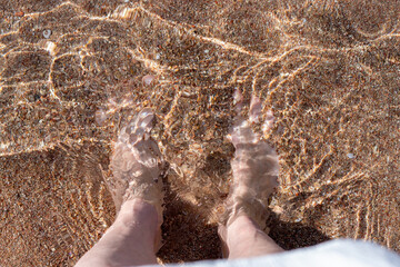 Legs of girl in the transparent sea on a sandy beach, top view