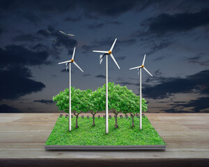 Obraz premium Wind turbines, trees, grass and birds from an open book on wooden table over sunset sky, Business ecological energy concept