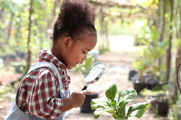 Happy African girl with black curly hair holding magnifying glass for exploring garden form, kid...