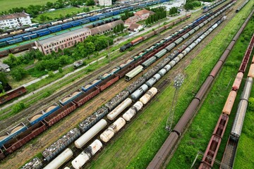 Aerial view above an industrial railroad yard with several freight train cars stationed on railroad...