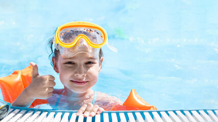 Close-up portrait of a cute little Caucasian girl swimming in the pool in a swimming mask and...
