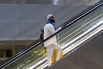 Young African American passenger man with yellow luggage stands on escalator, arrives from abroad,...