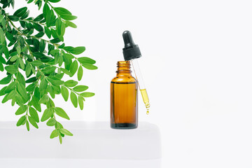 Natural medicine or aroma oil or beauty essence concept mockup vial with dropper with droplet on glass stand with green plant and white background. Face and body spa serum care concept banner