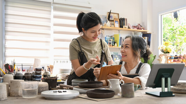 Two happy craft pottery shop owners checking product purchase order on laptop. Small business and art shop ownership