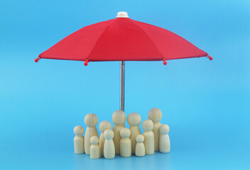 People protection, insurance and safety concept. Many wooden people figures under red umbrella on blue background.