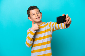Little boy isolated on blue background making a selfie with mobile phone