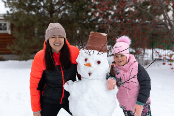 Smiling young girl and middle aged woman hugging snowman in daytime while having walk in park with...