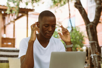 Smiling african american businessman working on laptop in the street cafe, crossing fingers and wishing good luck outdoors. Hope for good results at work. Professional conclusion of contract, finance