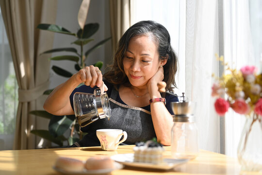 Pleased middle age woman preparing coffee for breakfast, spending free time in morning at comfortable home