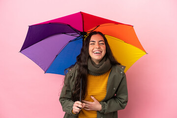 Young woman holding an umbrella isolated on pink background smiling a lot