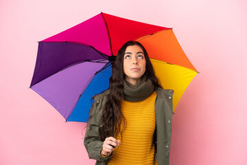 Young woman holding an umbrella isolated on pink background and looking up