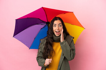 Young woman holding an umbrella isolated on pink background with surprise and shocked facial expression