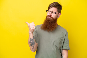 Redhead man with beard isolated on yellow background unhappy and pointing to the side