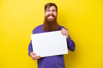 Redhead man with beard isolated on yellow background holding an empty placard with happy expression