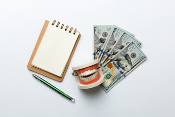 Flat lay composition with educational dental typodont model and money with notebook on colored table, top view. Expensive treatment