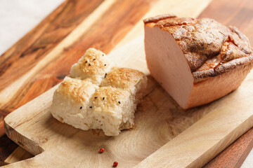 Traditional oven baked bavarian meal leberkäse sliced - meat dish made of corned beef, pork and bacon, finely ground and bakes as a bread loaf, on wooden board on dark wooden table with bread cubes