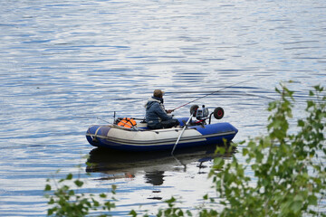 A man is a fisherman with a fishing rod on a rubber boat with a motor on the river. . High