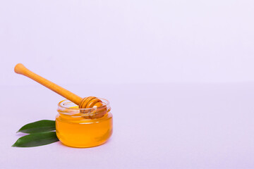 Honey in jar with leaves and honey dipper on colored background top view with copy text