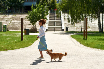 Girl running with Corgi dog on sidewalk in park