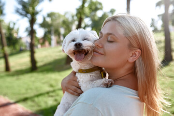 Smiling girl hugging Maltese dog in blurred park