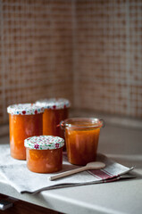 Four cans of freshly brewed orange-apricot jam on a linen towel with a wooden spoon.