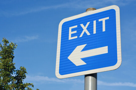 Naklejki Exit road sign with arrow symbol pointing to the left, against a clear blue sky.