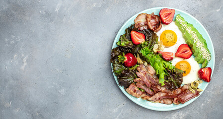 Plate with fried eggs, bacon, avocado, strawberries and fresh salad on a light background. Ketogenic diet food, healthy meal concept, Long banner format. top view